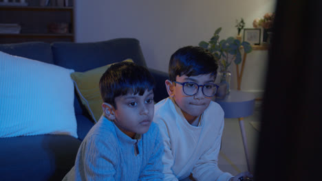 Two-Young-Boys-At-Home-Playing-With-Computer-Games-Console-On-TV-Holding-Controllers-Late-At-Night